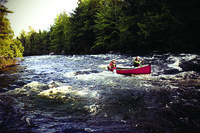 A color photograph of two paddlers going through rapids in a synthetic canoe.