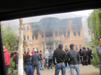 This is the prosecutor’s office that was burned down by the protesters. About fifty young male protesters are gathered in front of it. Burned debris is scattered on the asphalt.