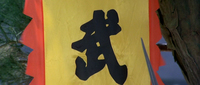 The black, calligraphic character for "warrior" or "military" is on a yellow banner, seen in closeup.