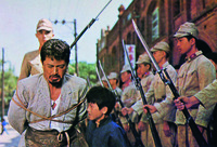 A shot from Victory showing a kneeling father waiting to be executed by Japanese soldiers, accompanied by his son.
