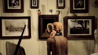 Fig. 13. Bare-chested black woman in kerchief, chained at neck to a bed. She faces back wall, looks in mirror; a colonial tableau with old photos on wall.