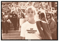 Young woman in foreground. Her white T-shirt reads, “NOT GOVERNMENT PROPERTY.” Around her, a huge crowd of women wearing buttons and carrying signs such as “KEEP ABORTION LEGAL.”