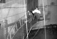 Two strolling players, one a comedian (left), the other a tragedian (right), slowly descend an elevated catwalk that curves around the stage and ends in the orchestra pit.
