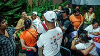 A man stands with his arm draped around a woman in the center of a group of journalists, including a television cameraman. Other women in the photograph are hugging and crying.