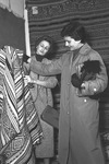 Two fashionable Israeli women with short haircuts examine a thick, decorative woolen Mizrahi fabric at the Maskit Village Craft Exhibition.