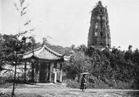 A black-and-white photo showing an old pagoda in the background to the right, an dilapidated pavilion in front to the left. A figure holding an umbrella stands to its right.