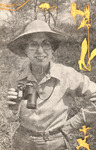 Three-quarter view. She stands, smiling, in a prairie with a broad-brimmed straw hat, glasses, and binoculars. She wears a checkered, long-sleeved shirt and jeans.