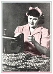 Pesotta sits at a sewing machine working on a piece of fabric. She wears a striped dress and her hair is tied with a scarf.