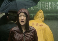 A woman in a raincoat faces the camera in the rain. Calligraphy can be seen on the yellow coat and the wall behind her.