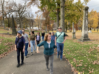 Color photograph showing group of nine members of the Pennsylvania Chapter of the Association for Gravestone Studies walking uphill in Allegheny Cemetery in Pittsburgh, flanked by monuments of different sizes and styles on either side.