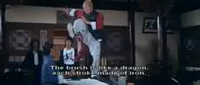 A man high kicks on a desk with black calligraphy framed on the wall behind him. White English subtitles are superimposed over it.
