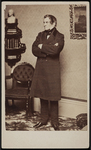 Circa 1860 studio portrait of Dr. Jacob Bigelow. He appears as a serious-­looking man with dark hair and arms crossed wearing a long suit coat, standing in a study with chair and corner bookcase with books and a marble bust behind him.