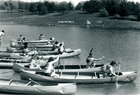 A black-and-white photograph of a canoe race in progress.