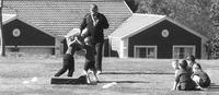 Two five-year-old boys wrestle while an adult supervises. Four other young boys sit on the ground.