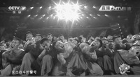 Film still depicting a dense group of kneeling actors, with their faces contorted and bright stage lights overhead center.