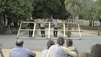 Color screenshot from a documentary film showing four male dancers, two are people with Down syndrome, as together they lift a large wooden frame upright in an open outdoor area.