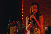 A shot from Drifting Flowers showing a young girl holding the microphone on a stand onstage.