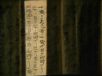 Pages of parchment have black calligraphy written on them, with a sliver of light falling vertically on it.