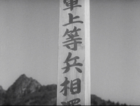 Calligraphy is written on a wooden stake outdoors, zoomed in with a mountainous background.