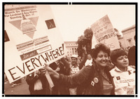 Two women in the foreground wear March on Washington T-shirts. One smiles with her arm around the other. Behind them is a crowd. One man smiles and signs “love.”