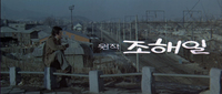 A dominant line of white calligraphy is centered above subordinate white characters in a second line. The calligraphy is superimposed on an establishing shot of the city. In the foreground is a man in a trench coat overlooking it.
