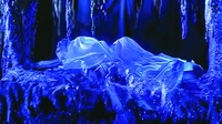 A color film still in a long shot showing a figure lying on a platform in a cave. Illuminated by a dark blue light, a woman in her translucent robe emerges as the giant snake fades from the platform.