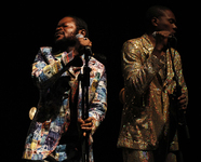 Fig. 16. Two male nightclub singers at microphones. One clad in glittery suit, the other in a jacket that looks like it’s made of money. Both look offstage.