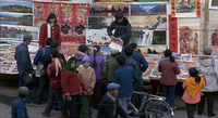 People gather along the street, looking at numerous posters and calligraphy banners on display on the wall and tables.