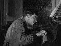 Figure 4. Canadian virtuoso pianist Glenn Gould, dressed in a bathrobe, hunches over his instrument and smiles, displaying his eccentric persona.
