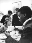 Three people sitting and eating at a table. The Guinean student is in the foreground, pictured mid-­bite.