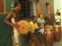 A still from a film showing drummers set up on sidewalk in front of the Ballumbrosio home for performance with the elder Ballumbrosio on the far right.