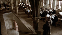 A series of monks sit in front of open books reading.