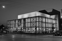 A large square building at the corner of a street. On the front facade hangs a promotional banner for the Kalamata International Dance Festival.