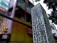 A documentary image of an electric box with graffito by the King of Kowloon. A trolley passes by in the background.