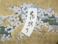The title calligraphy for _Breaking of Branches is Forbidden_ is written on a curious, curved strip of white paper. It lays over what appears to be a fusama screen with a lush painting of cherry blossoms on gold leaf.