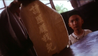 A man shows a scroll to a boy with white calligraphy on it.