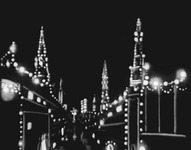 Film still depicting the illuminated outlines of city buildings against a completely dark background.