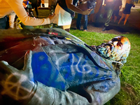 Photograph of a statue of Confederate general Albert Pike that has been toppled and is lying on its side on the grass.