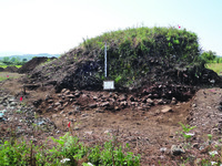 Photograph of a tumulus surrounded by cobbles and dirt.