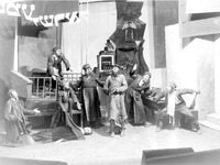 Black-and-white photograph of a group of actors in exaggerated poses with Hebrew letters hanging above them