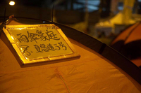 This photograph shows a laminated sign with the address Number 3, Harcourt Road, Umbrella Villa in Chinese attached to a tent