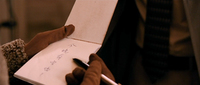 Blue calligraphy is written on a notepad in closeup.Gloved hands hold the notebook.