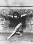 Figure 4.1. Murayama Tomoyoshi in bobbed hair and a dress stands barefoot and barelegged, arms spread like eagle wings, leaning and staring forward in front of a stone fireplace.