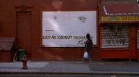 A character writest graffito on a framed area for posters: "Like an ignorant East Suit." The adjacent storefront has an awning saying "Sanchez Grocery," the name rendered cursively to evoke a signature.