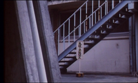 A white public placard in front of a staircase has black calligraphy written on it.