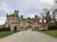 Color photograph of Tudor-­style gateway and Gothic Revival chapel tower at Allegheny Cemetery in Pittsburgh with wide driveway to the entrance in the foreground.