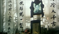 Black calligraphy on vertical banners hang around a black-wreathed portrait and offerings.