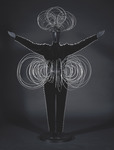 Black-and-white photograph of a costume for the Triadic Ballet, Wire Figure, with spirals of metal wires that create a large abstracted tutu and a large spiraling headdress. The mannequin stands with arms stretched outward and upward, also wearing a black bodysuit lined with metal beads.