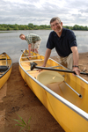 A color portrait of Mike Cichanowski next to a group of Kevlar canoes on the shore.