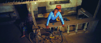 Film still frame of man leaning on veranda rail outside a small house